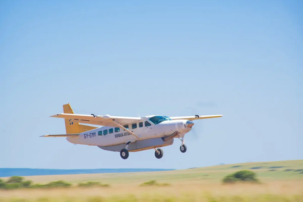 a plane across the golden plains of the Masai Mara, with a herd of topi antelope grazing nearby, on a 3-day fly-in safari from the Kenya coast with Ahot Sun Safaris.